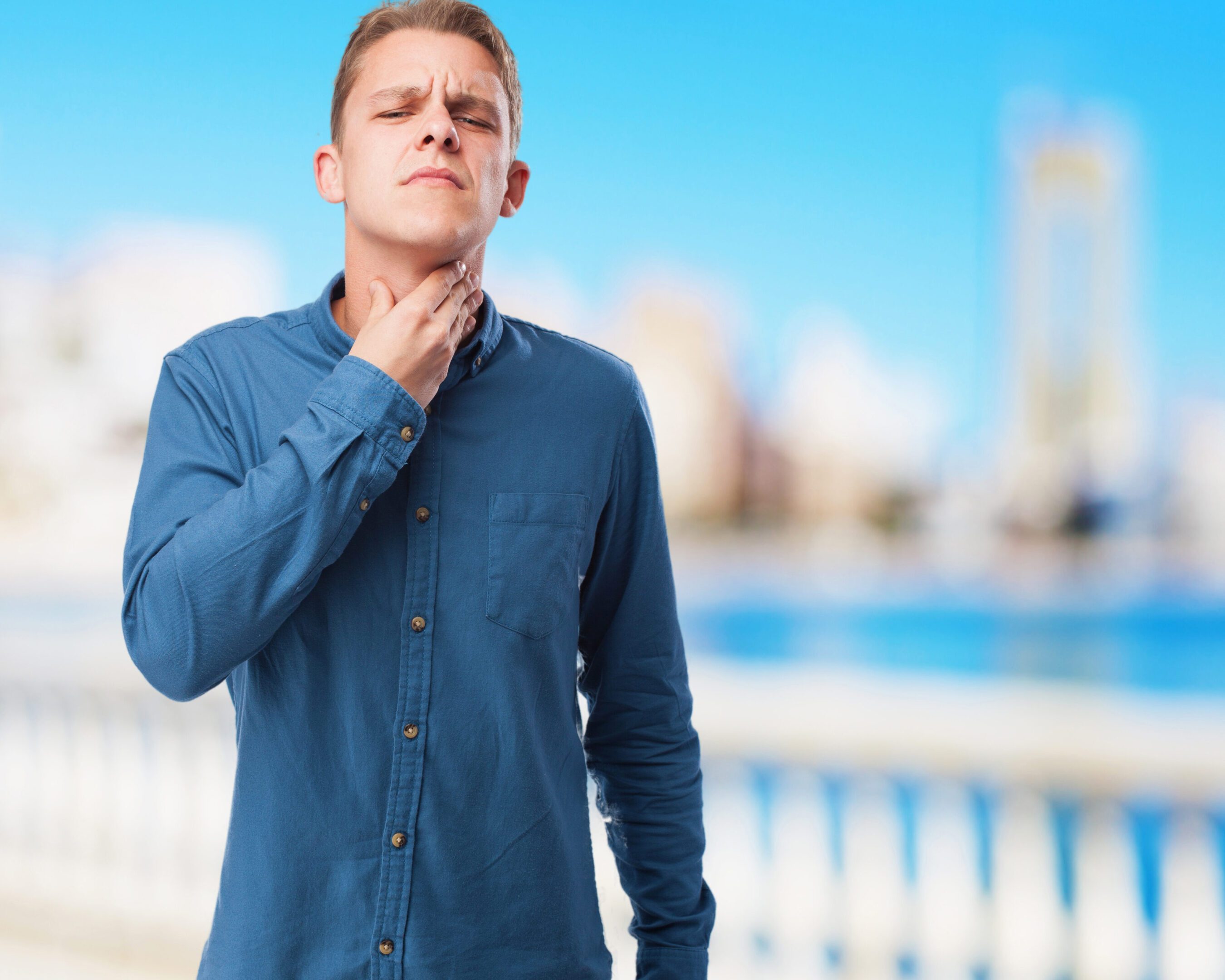 Young man touching his throat outdoors, looking uncomfortable.