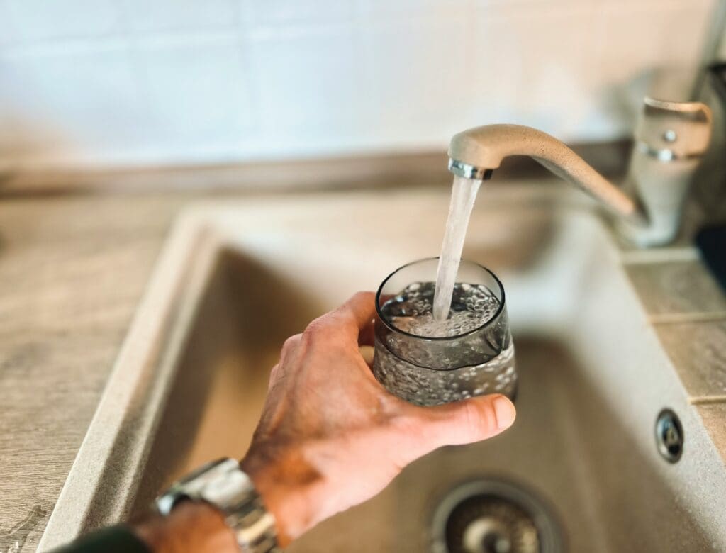 Man in Raleigh NC kitchen filling glass with well water, illustrating hidden heavy metal exposure